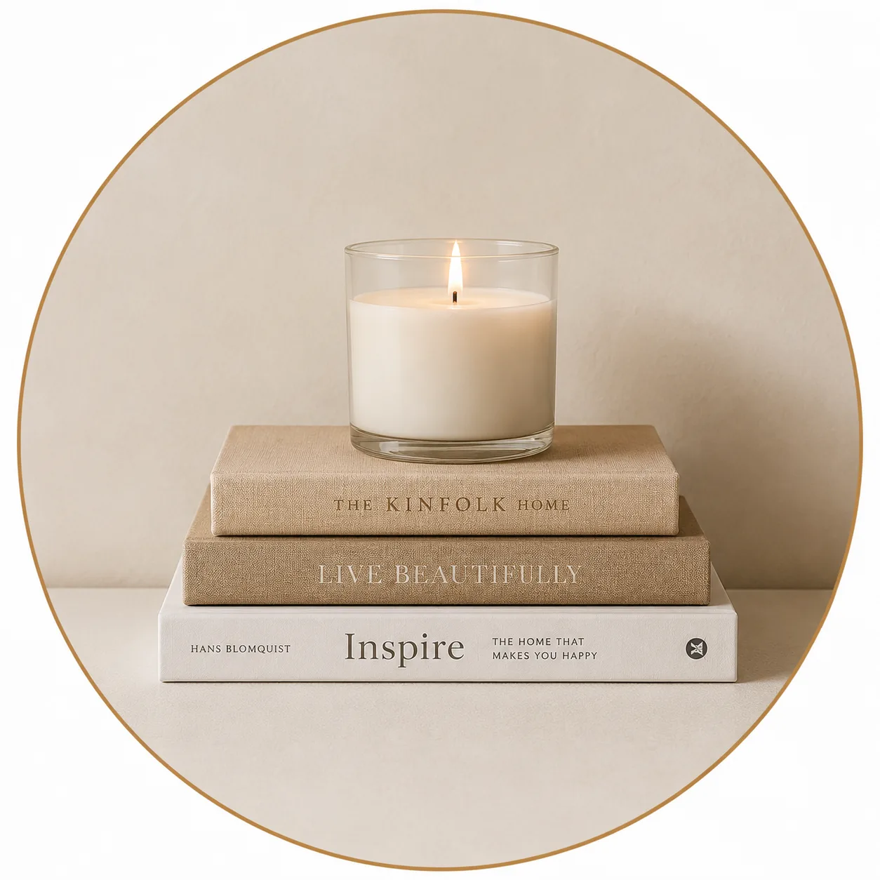A clean glass candle lit on top of a stack of neutral hardcover design books including The Kinfolk Home and Live Beautifully.